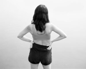 Mimi Plumb The Reservoir Back view of a woman in a sports bra top standing on the edge of a lake