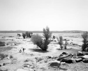 Mimi Plumb The Reservoir Black and white photograph of family carrying inner tubes across dry lake bed.